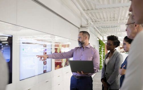 Businessman with laptop leading meeting at screen in office